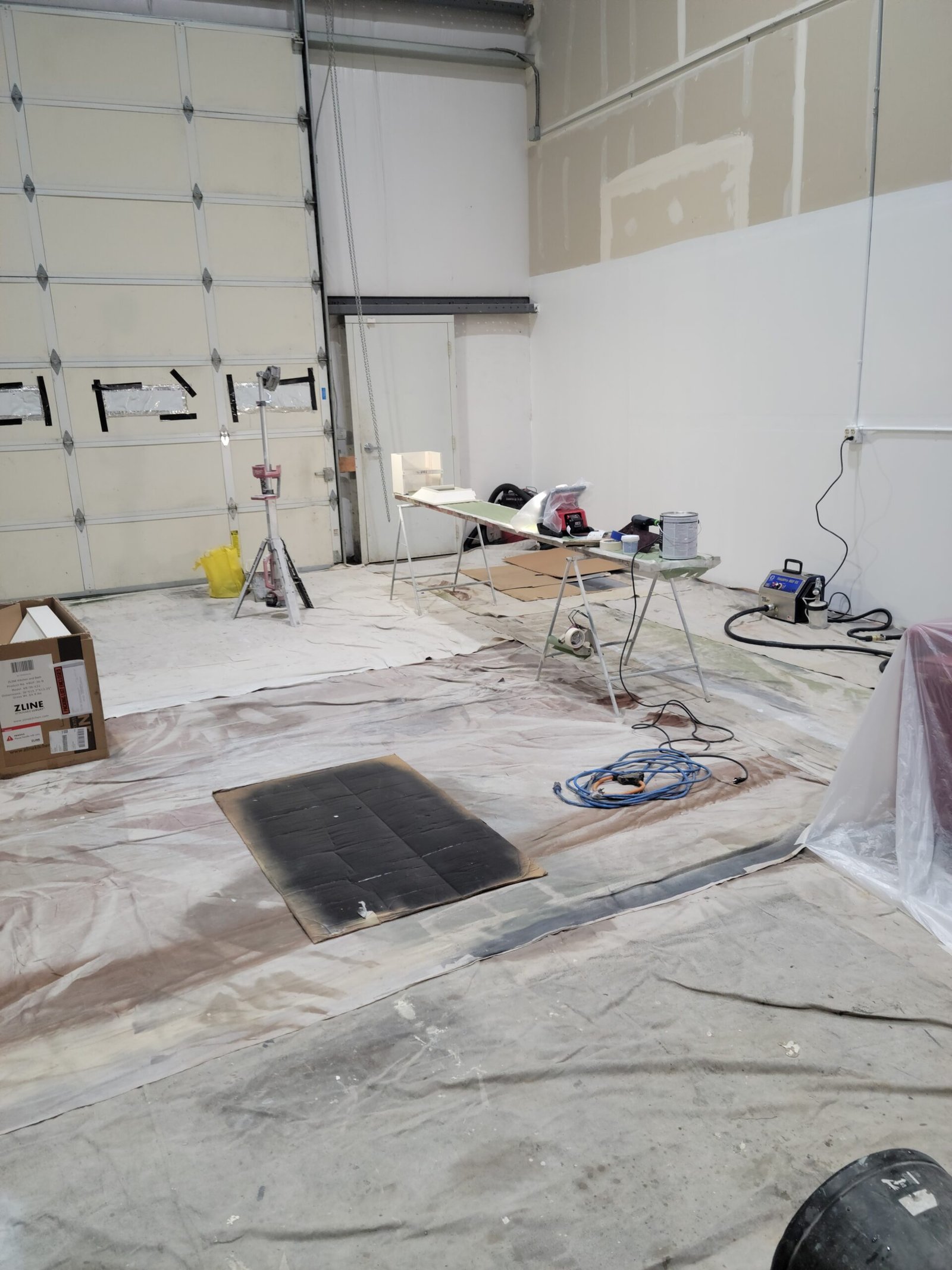 Interior work area with protective floor coverings, painting equipment, and walls being prepared